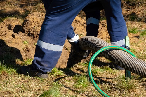 Man worker holding pipe, providing sewer cleaning service outdoo
